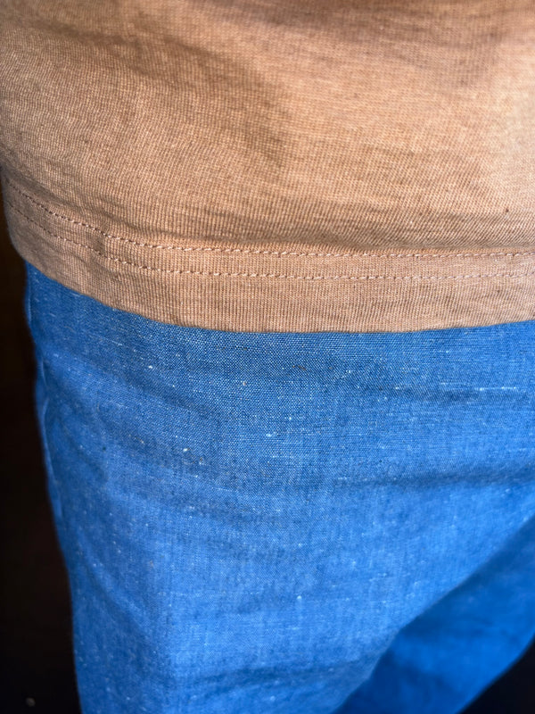 Close-up of a person wearing a tan knit top and blue denim shorts, showing the hem of the top and the fabric of the shorts.