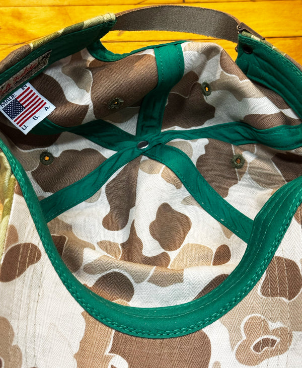 Close-up of the inside of a baseball cap with a brown, beige, and white camouflage pattern, green trim, and a visible 'Made in USA' label.