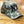 A baseball cap with a green, brown, and beige camouflage pattern, featuring a large black embroidered 'NY' logo on the front, displayed on a wooden floor.