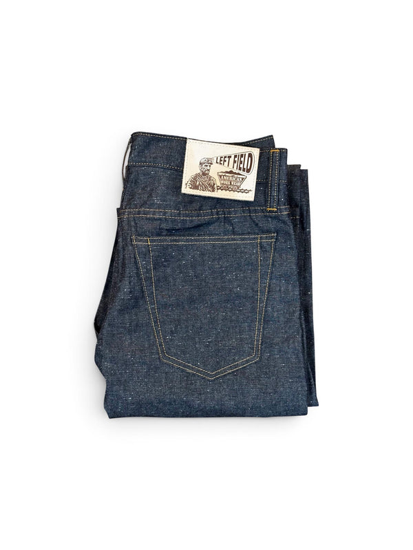 A pair of folded dark blue denim jeans with a visible 'The Left Field' brand patch on the back waistband, shot against a plain white background.