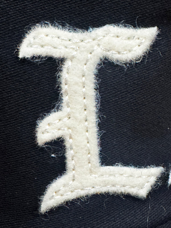 A close-up of a white embroidered letter 'I' patch on a black fabric background.