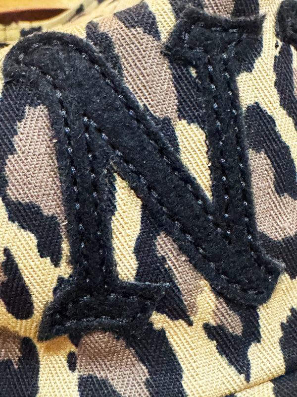 Close-up of a black embroidered letter 'N' patch applied to a beige, brown, and black camouflage patterned fabric.